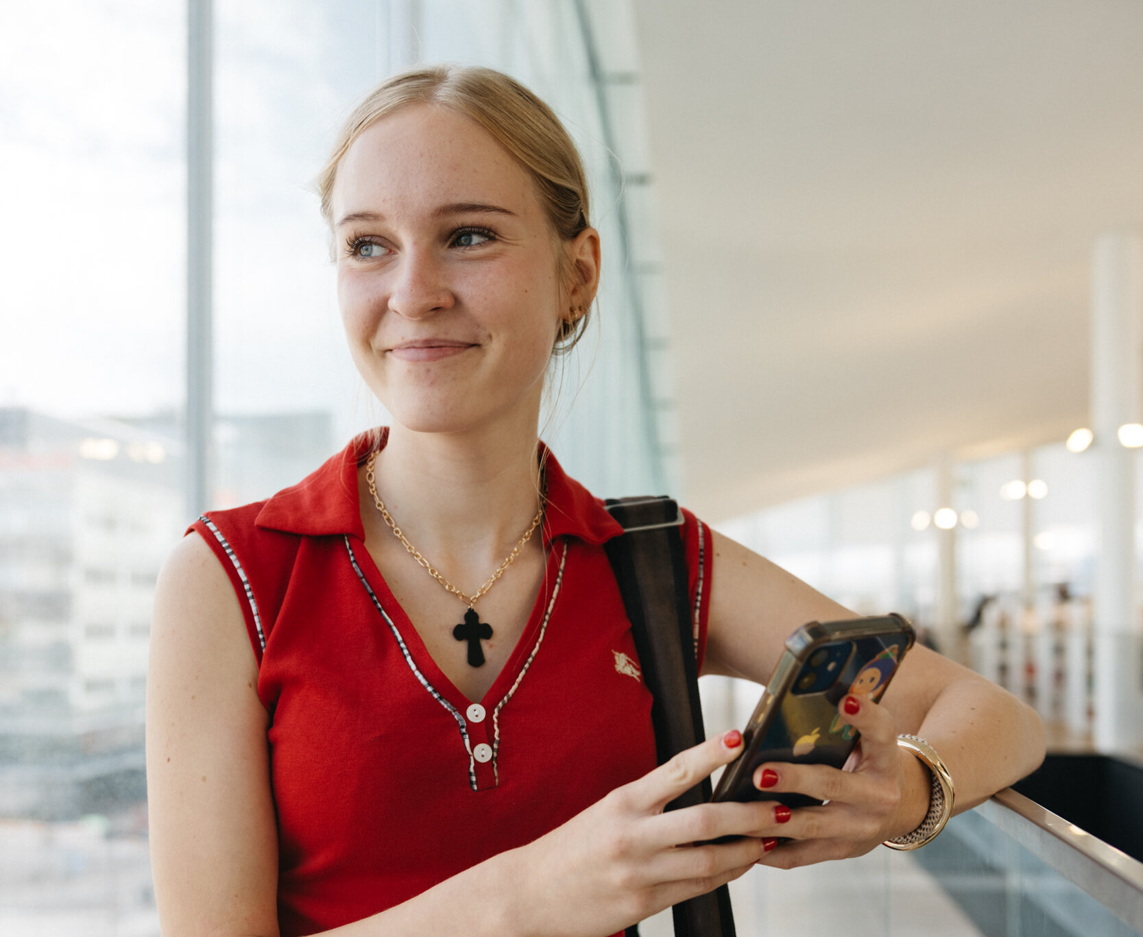 Hymyilevä tyttö katsoo kaukaisuuteen puhelin kädessä